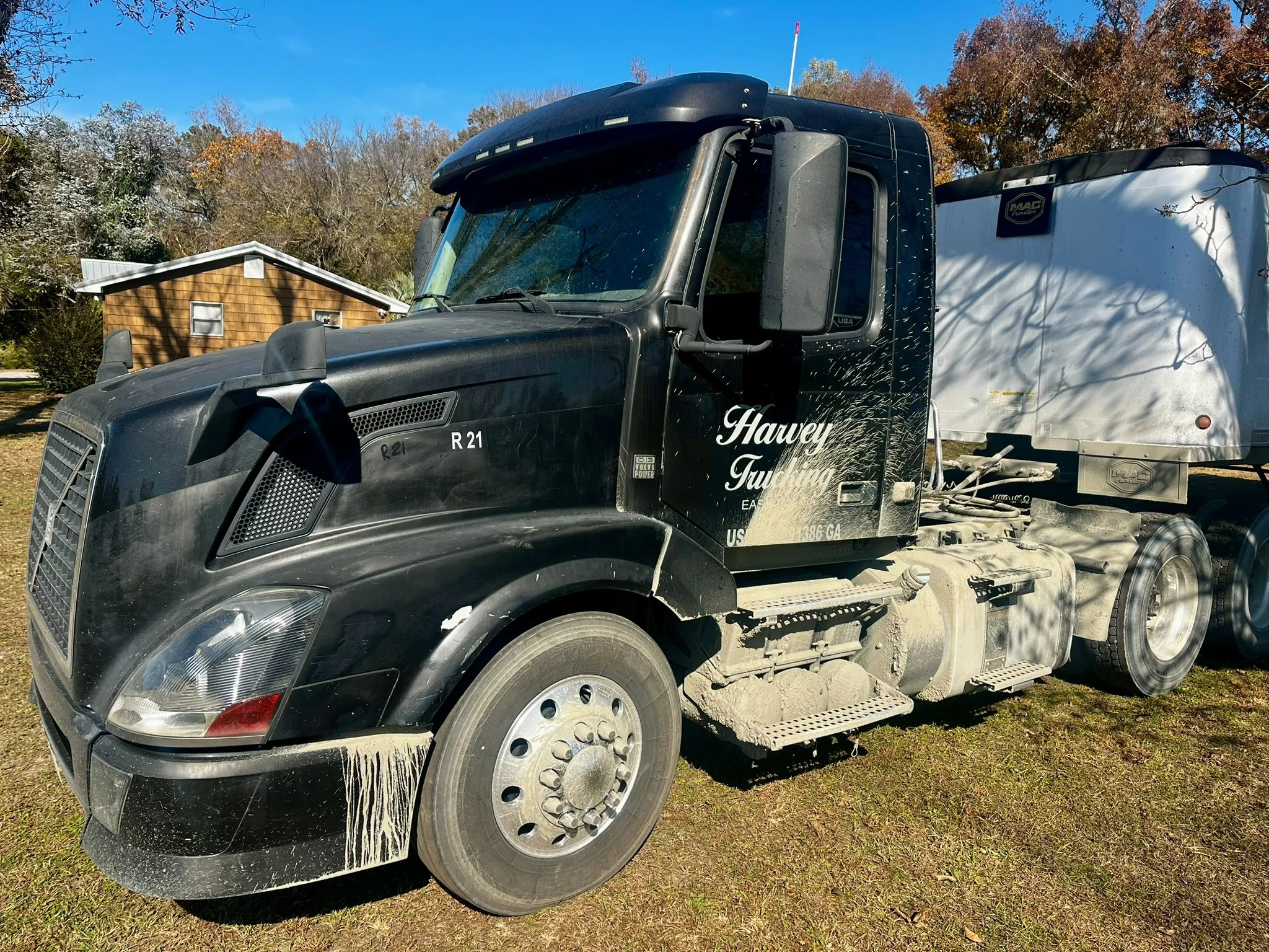 Black commercial tractor and trailer before wash, with heavy dirt on steps and fuel tank